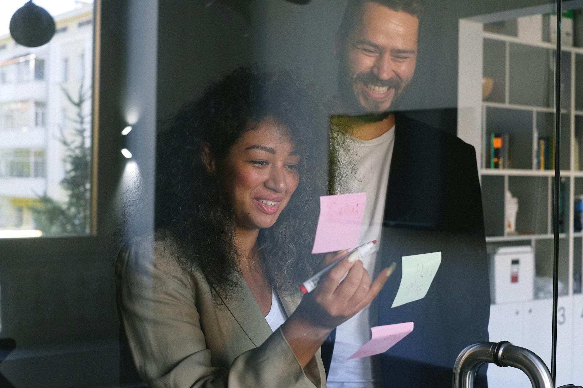 Diverse happy business partners checking stickers on glass door and smiling together in office