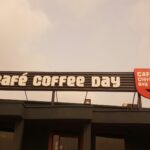 Close-up of the Café Coffee Day sign under a cloudy sky, located in Coimbatore, India.