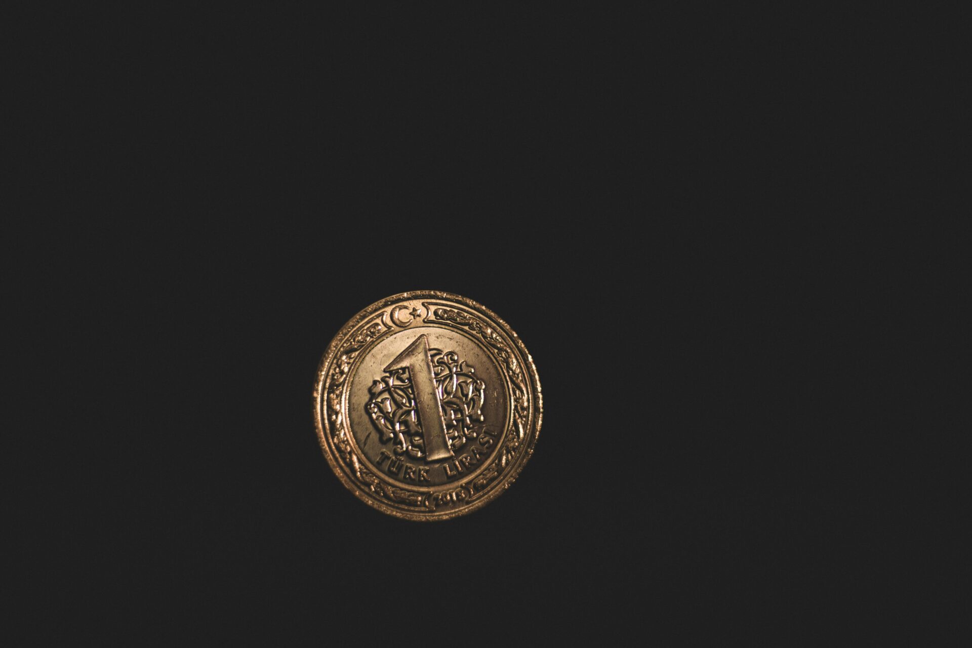 Minimalist close-up of a gold Turkish lira coin on a dark background, symbolizing economy.