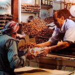 Two men exchanging dates in a vibrant Dubai spice market stall.