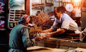 Two men exchanging dates in a vibrant Dubai spice market stall.